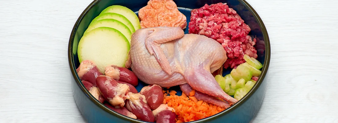 A bowl of fresh raw dog food: whole quail, ground meat, organ meat, zucchini, carrot, celery, and sweet potato